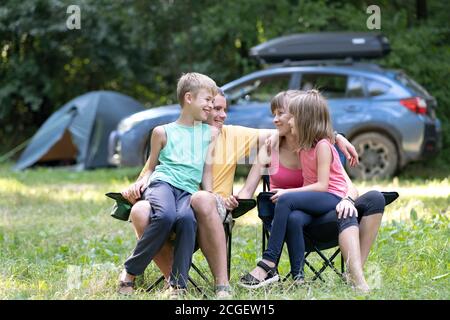 Vater, Mutter und ihre Kinder genießen Zeit auf dem Campingplatz im Freien. Eltern und ihre Kinder sitzen zusammen und unterhalten sich glücklich. Stockfoto