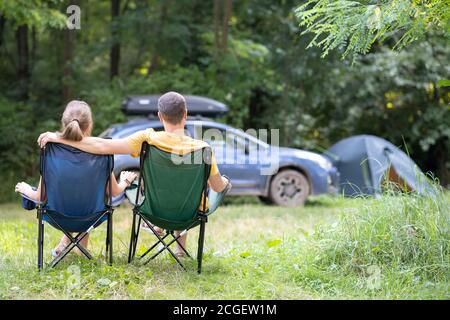 Ein glückliches Paar sitzt auf Stühlen auf dem Campingplatz und umarmt sich. Reise-, Camping- und Urlaubskonzept. Stockfoto