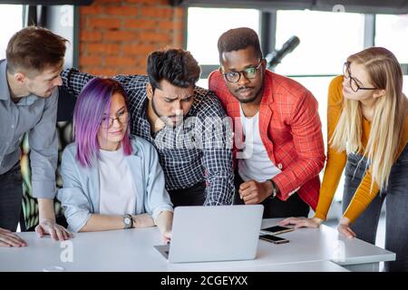 Multi-Ethnic Gruppe von Menschen, die in der Nähe von Frau mit violettem Haar, gemeinsam mit ihrem Laptop, lesen alle zusammen erstaunliche Nachrichten. Stockfoto