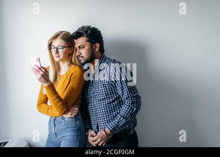 Romantische multiethnischen Paar Auswahl Badeort für ihre Flitterwochen mit Smartphone. Studio isolierte Schuß über grauer Hintergrund mit Copyspace. Stockfoto