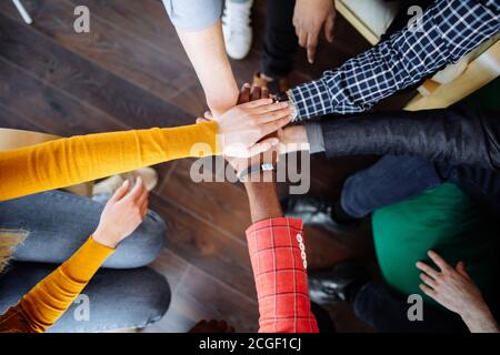 Nahaufnahme der freigeschnittenen menschlichen Hände in verschiedenen bunten Kleidung verbindet sich in Teamgeist hoch fünf über Holzhintergrund, Weitwinkel-Aufnahme Stockfoto