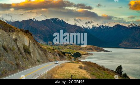 Ein Auto lief auf einer Straße am Seeufer. Der Hintergrund ist ein toller Berg am Abend. Schöne Wolken am Hawea See Aussichtspunkt in Wanaka Ota Stockfoto