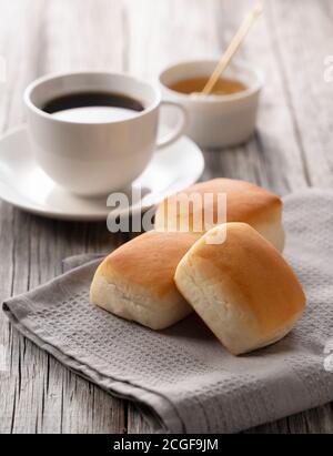 Vor einem alten Holzhintergrund werden Brötchen, Kaffee und Honig serviert. Bild Frühstück. Stockfoto