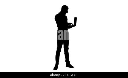 Silhouette junger mittelöstlicher Geschäftsmann, stehend und tippend auf Laptop, wenn er es in den Händen hält. Stockfoto