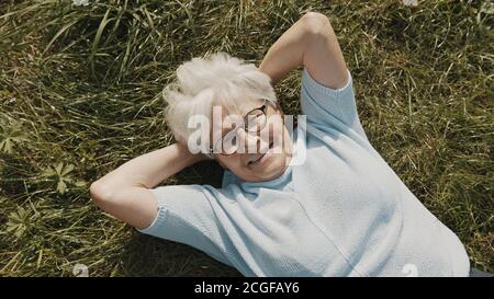 Ältere Frau, Rentnerin auf dem Gras liegend mit den Händen unter dem Kopf im Garten oben Nahaufnahme. Hochwertige Fotos Stockfoto