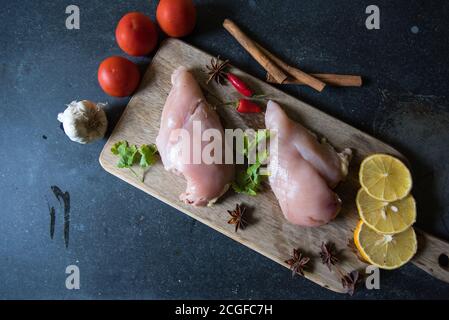 Rohe Hähnchenfilets auf einem Holzschneidebrett mit Zutaten Zum Kochen auf schwarzem Hintergrund Stockfoto