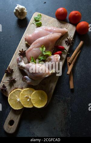 Draufsicht auf rohe Hähnchenschenkel mit Gewürzen auf einem Platte auf schwarzem Hintergrund Stockfoto