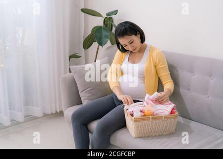 Eine schwangere Frau, die auf einem Sofa sitzt und die Dinge für die Geburt eines Kindes vorbereitet. Stockfoto