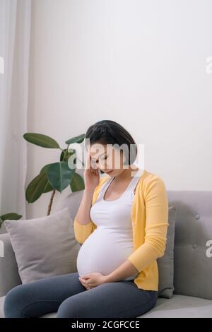 Junge schwangere Frau mit Kopfschmerzen zu Hause Stockfoto