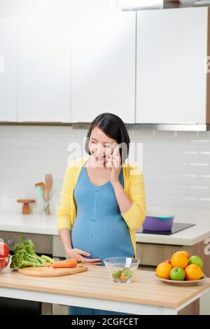 Glückliche schwangere Frau, die auf dem Smartphone anruft und beim Frühstück ansteht Wohnküche Stockfoto