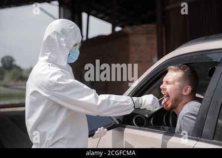 Konzept Verbot Fahrer Auto Reise Coronavirus. Arzt in schützenden Virusanzug, der Tupfer vom Mann nimmt, um auf COVID-19-Infektion zu testen Stockfoto