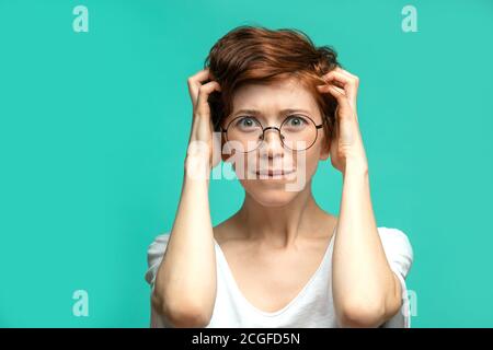 Frustriert oder unzufrieden rothaarige kaukasische Frau, die die Arme auf dem Kopf hält, im Dispare, als ob sie etwas irreparable tat, Blick auf Kamera-Isol Stockfoto