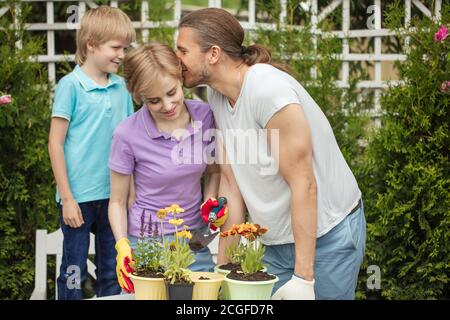 Liebevolle Eltern mit Sohn Pflanzen Blumen in Töpfen in Pflanzfarm . Junge hilft Eltern. Gartenbau. Blumenzucht. Blumen Pflanzen. Gartengeräte Stockfoto