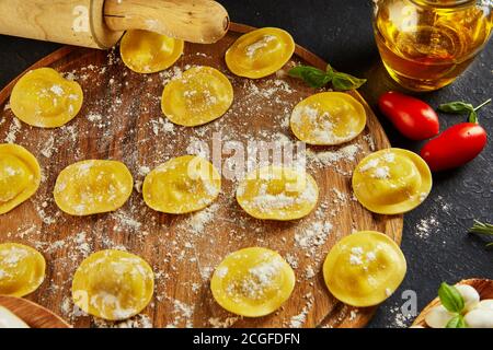 Leckere Ravioli mit Mehl, Kirschtomaten, Sonnenblumenöl und Basilikum auf dunklem Grund. Der Prozess der Herstellung von italienischen Ravioli. Stockfoto