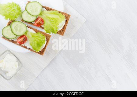 Frischer Sommer gesunde Vorspeise aus Vollkorn Roggen Chips Brot mit Gemüse - grüner Salat, Gurke, Tomaten, Frischkäse auf weißem Holzbrett, Top Stockfoto