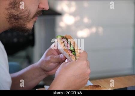 Nahaufnahme eines jungen Mannes, der ein Pastrami-Sandwich isst. Fast-Food-Konzept. Stockfoto