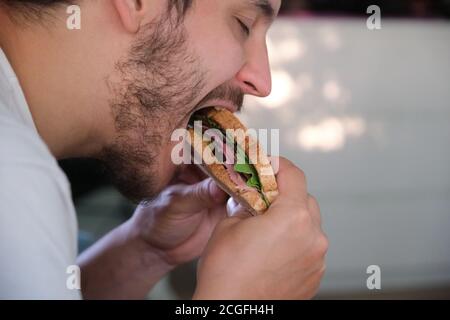 Nahaufnahme eines jungen Mannes, der ein Pastrami-Sandwich isst. Fast-Food-Konzept. Stockfoto