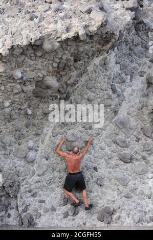 Mann übt Alpinismus, während er eine vertikale Felswand klettert Stockfoto