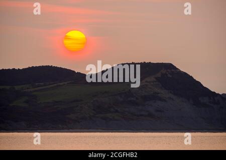 Lyme Regis, Dorset, Großbritannien. September 2020. Wetter in Großbritannien. Blick von Lyme Regis in Dorset bei Sonnenaufgang, wenn die Sonne durch die dünne Wolke von hinter Golden Cap an der Jurassic Coast aufgeht. Bild: Graham Hunt/Alamy Live News Stockfoto