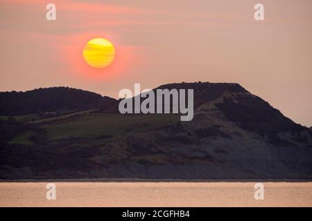 Lyme Regis, Dorset, Großbritannien. September 2020. Wetter in Großbritannien. Blick von Lyme Regis in Dorset bei Sonnenaufgang, wenn die Sonne durch die dünne Wolke von hinter Golden Cap an der Jurassic Coast aufgeht. Bild: Graham Hunt/Alamy Live News Stockfoto