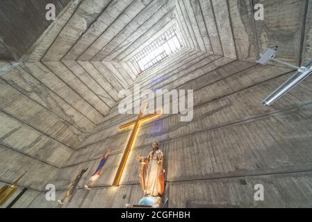 Blick auf den Kamin-ähnlichen Turm, vom Altar, Kruzifix und Statue von Jesus, zu einem hohen Fenster Licht, atemberaubende brutalistischen kommunistischen Ära Design, com Stockfoto