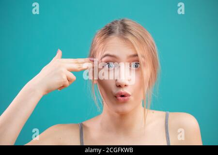 Porträt einer müden oder gelangweilten kaukasischen Frau, verärgert oder gestört mit lauter Musik aus dem Nachbarzimmer, machen Waffe Geste, als sie sich schießen Stockfoto