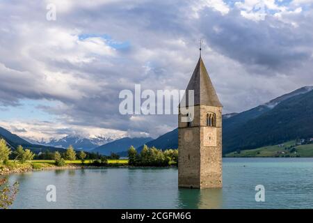 Der berühmte Glockenturm des alten Graun, untergetaucht im Reschensee, Südtirol, Italien, mit den schneebedeckten Alpen im Hintergrund Stockfoto
