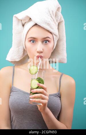 Attraktive erstaunt Frau mit Handtuch auf dem Kopf trinken grünen Bio-Cocktail durch einen Stroh, überrascht, wie lecker in sein kann. Isolierte Schussaufnahme Stockfoto