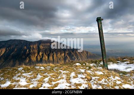 Eine Stange auf der Spitze des Berges gepflanzt. Im Hintergrund die von der Sonne beleuchtete Seite des Berges. Wolkiger Himmel. Alpe del Nevegal, Belluno, I Stockfoto