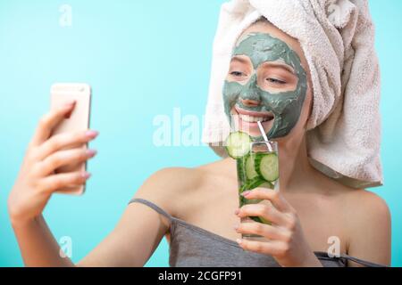 Nette Frau mit Handtuch auf dem Kopf, Spaß beim Arrangieren sich für eine Tanzparty, Selfie mit Ton Schönheitsmaske auf Gesicht zu tun. Stockfoto