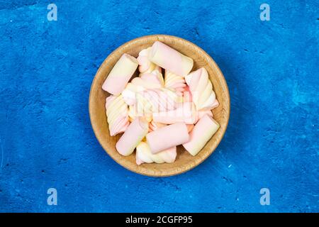 Gelbe und rosa Marshmallows in einer Holzschale und weiter Ein klassischer blauer Hintergrund Stockfoto