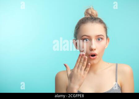 Überrascht beschupfte kaukasische Mädchen bedeckt ihren Mund mit der Hand und hält ihre Augen weit offen. Casual Frau sagen wow auf einem blauen Hintergrund erstaunt sein Stockfoto