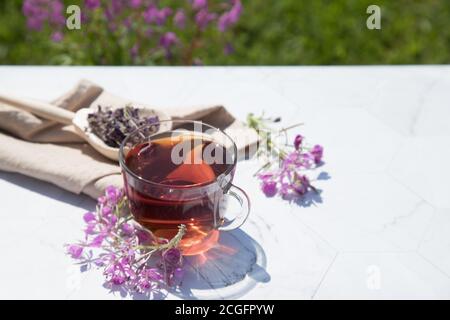 Kräutertee aus fermentierten Kipreya-Blättern in einer Glasschale auf hellem Hintergrund liegt das Gebräu in einem Holzlöffel auf einer beigen Serviette.Traditionelles russisches K Stockfoto