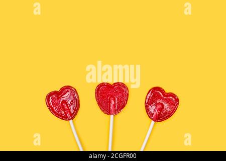 Drei rote herzförmige Lutscher auf gelbem Hintergrund Stockfoto