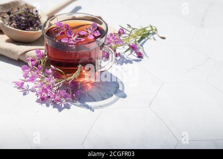 Kräutertee aus fermentierten Kipreya-Blättern in einer Glasschale auf hellem Hintergrund liegt das Gebräu in einem Holzlöffel auf einer beigen Serviette.Traditionelles russisches K Stockfoto