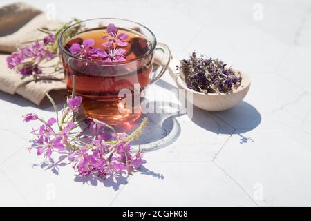 Kräutertee aus fermentierten Kipreya-Blättern in einem Glas Tasse auf einem hellen Hintergrund liegen getrocknete Blumen in einem Holzlöffel daneben.Traditionelles russisches Kopo Stockfoto