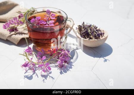 Kräutertee aus fermentierten Kipreya-Blättern in einem Glas Tasse auf einem hellen Hintergrund liegen getrocknete Blumen in einem Holzlöffel daneben.Traditionelles russisches Kopo Stockfoto