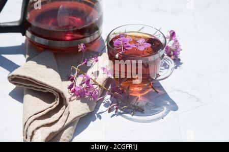 Kräutertee aus fermentierten Kipreya-Blättern in einem Glas Tasse auf einem hellen Hintergrund steht eine Teekanne mit Tee daneben.Traditioneller russischer Kopor-Tee (Ivan Stockfoto