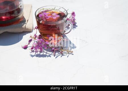 Kräutertee aus fermentierten Kipreya-Blättern in einem Glas Tasse auf einem hellen Hintergrund steht eine Teekanne mit Tee daneben.Traditioneller russischer Kopor-Tee (Ivan Stockfoto