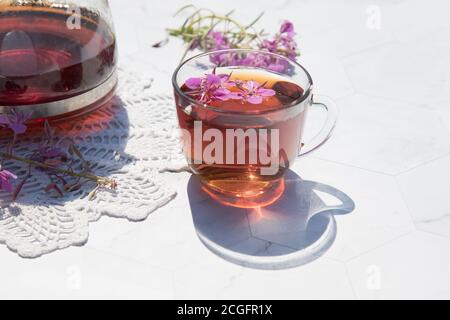 Kräutertee aus fermentierten Kipreya-Blättern in einer Glasschale auf hellem Hintergrund steht daneben eine Teekanne mit Tee auf einer Spitzenserviette.Traditionelles Russland Stockfoto