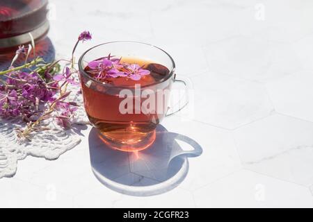 Kräutertee aus fermentierten Kipreya-Blättern in einer Glasschale auf hellem Hintergrund steht daneben eine Teekanne mit Tee auf einer Spitzenserviette.Traditionelles Russland Stockfoto