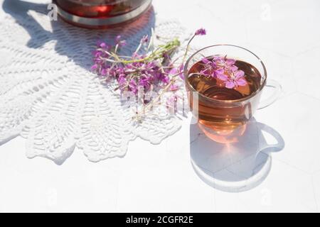 Kräutertee aus fermentierten Kipreya-Blättern in einer Glasschale auf hellem Hintergrund steht daneben eine Teekanne mit Tee auf einer Spitzenserviette.Traditionelles Russland Stockfoto