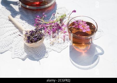 Kräutertee aus fermentierten Kipreya-Blättern in einer Glasschale auf hellem Hintergrund steht daneben eine Teekanne mit Tee auf einer Spitzenserviette.Traditionelles Russland Stockfoto