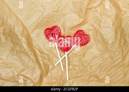Drei rote herzförmige Lutscher auf faltenbraunem Papier In einer Draufsicht Stockfoto