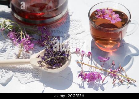 Getrockneter Kräutertee aus fermentierten Kipreya-Blättern in einem Holzlöffel auf hellem Hintergrund steht eine Teekanne mit Tee und einem transparenten Becher daneben auf einem Stockfoto