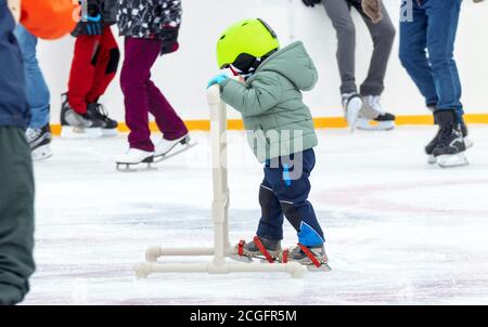 Schwierigkeiten der ersten Schritte auf Schlittschuhe. Kind macht erste Schritte auf Schlittschuhe mit Hilfe in Eisbahn. Stockfoto