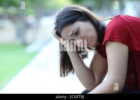 Traurige Frau, die auf einer Bank in einem Park sitzt und sich beschwert Wegschauen Stockfoto