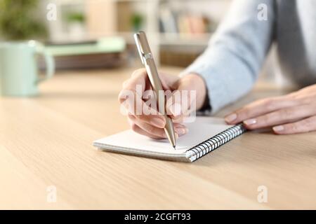 Nahaufnahme einer Frau Hand witing auf einem Notizblock Sitzen auf einem Schreibtisch zu Hause Stockfoto