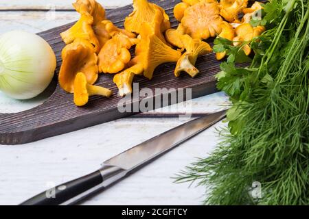 Pfifferlinge liegen auf einem dunklen Holzbrett, ein Zwiebelkopf und ein Dill liegen auf dem Tisch. Der Herbst kommt Stockfoto