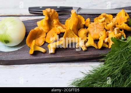 Pfifferlinge liegen auf einem dunklen Holzbrett, ein Zwiebelkopf und ein Dill liegen auf dem Tisch. Der Herbst kommt Stockfoto